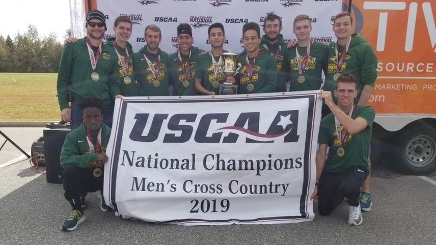 Men's cross country holding their fourth consecutive USCAA national championship banner. 