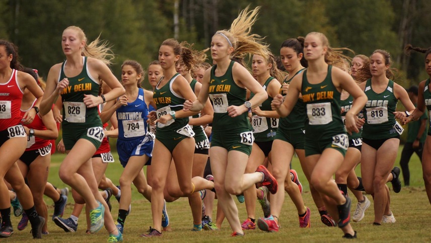 The women's cross country team runs out of the starting line. 