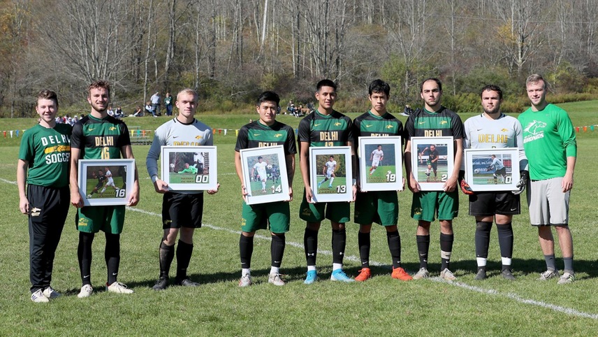 The graduating men's soccer pose with their commemorative photos alongside Coach Mitko and Coach Akey.