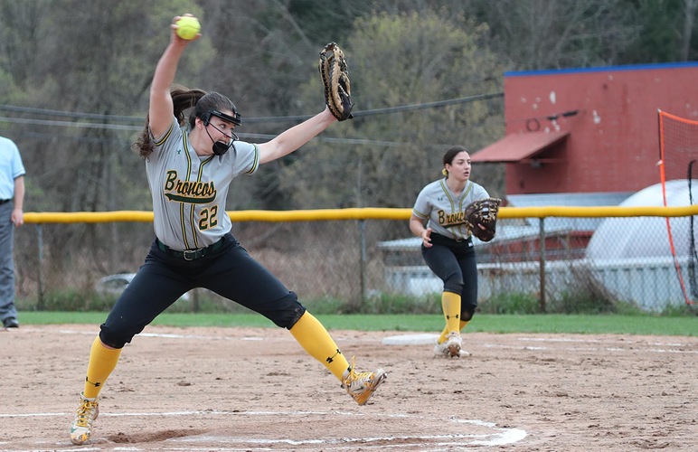 Haylee Lefebvre delivering a pitch, with first baseman Mackenzie Sparacino looking on. 