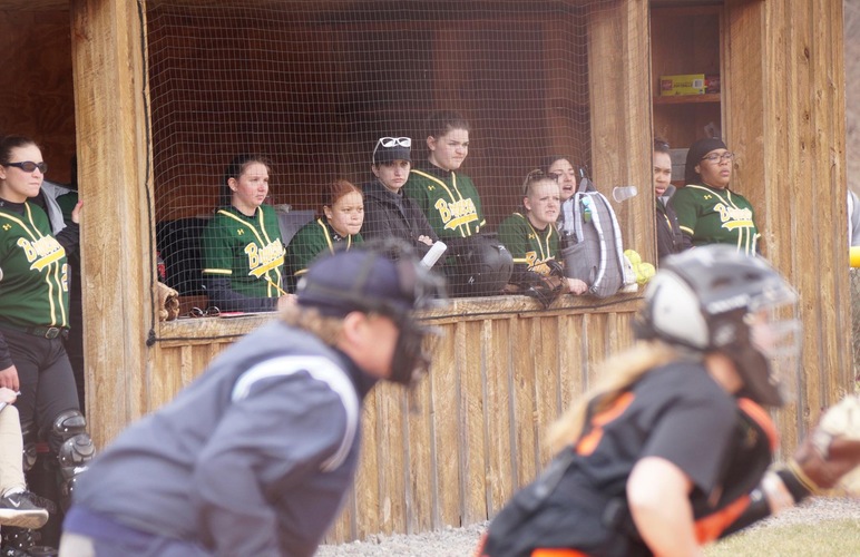 Softball team in the dugout cheering on their teammates at bat. 