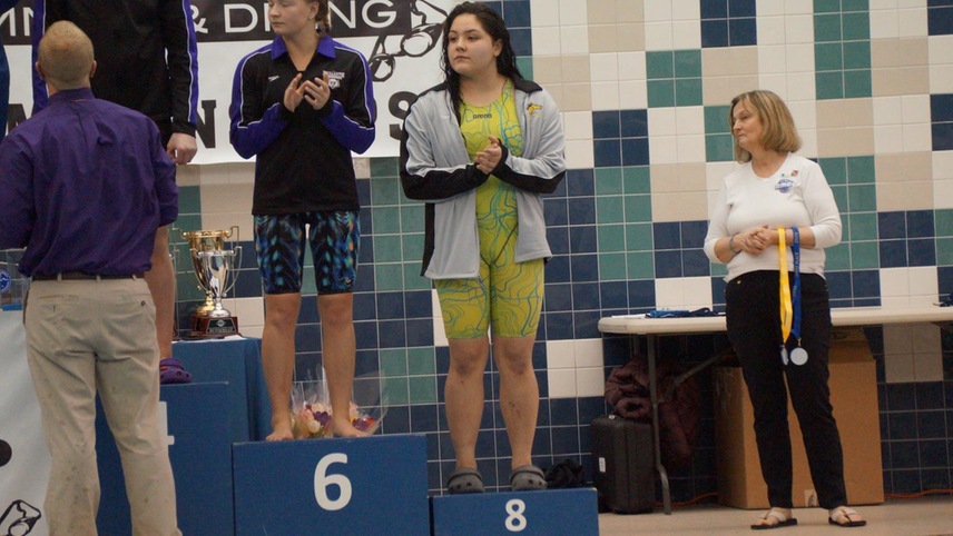 Kaitlyn Quezada standing on the eighth-place podium after competing in the 100-yard freestyle.
