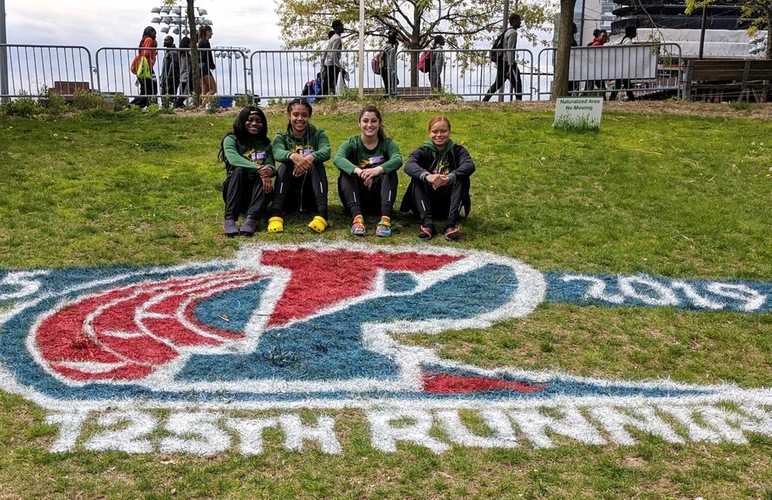 The women's 4x100 team posing next to the 2019 Penn Relays grass-painted signage. 