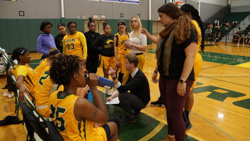 The women's basketball team huddles during a timeout on the bench,