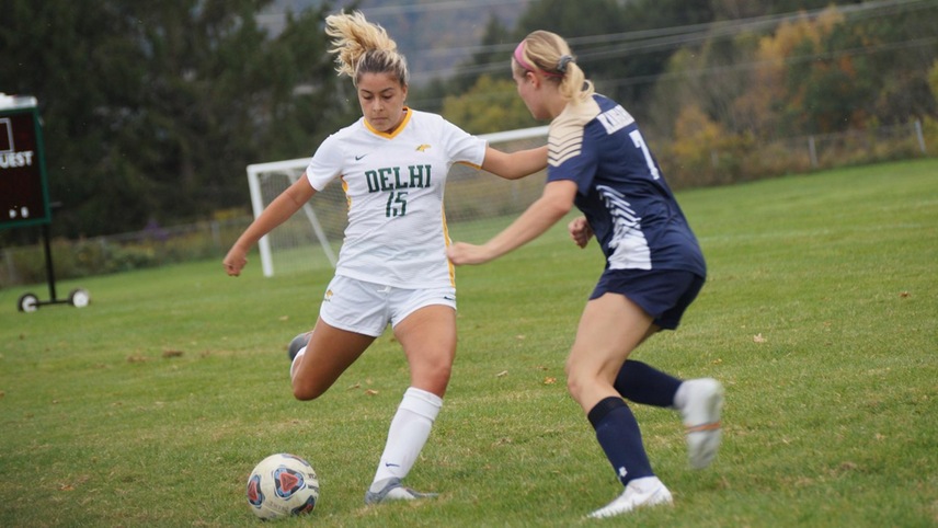 Sarah Mojica kicking the ball with a SUNY Canton player in front of her.