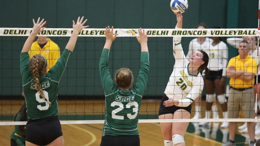 Chloe Elsenbeck hitting the ball over the net with two players in front of her.
