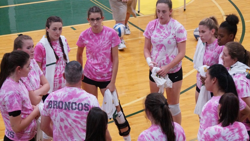 The volleyball team in a group huddle prior to a match wearing pink tie-dye shirts.